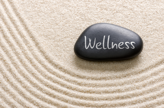 w rock with the word "wellness" on it lying on a layer of white sand